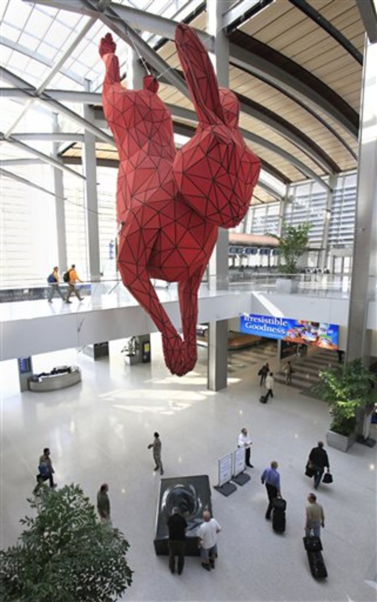 In this photo taken Wednesday Oct. 19, 2011, visitors pass under a 56-foot red rabbit that spans two floors at Sacramento International Airport in Sacramento, Calif. The bunny, titled " Leap" by Denver-based artist Lawrence Argent, has drawn mixed reviews. 